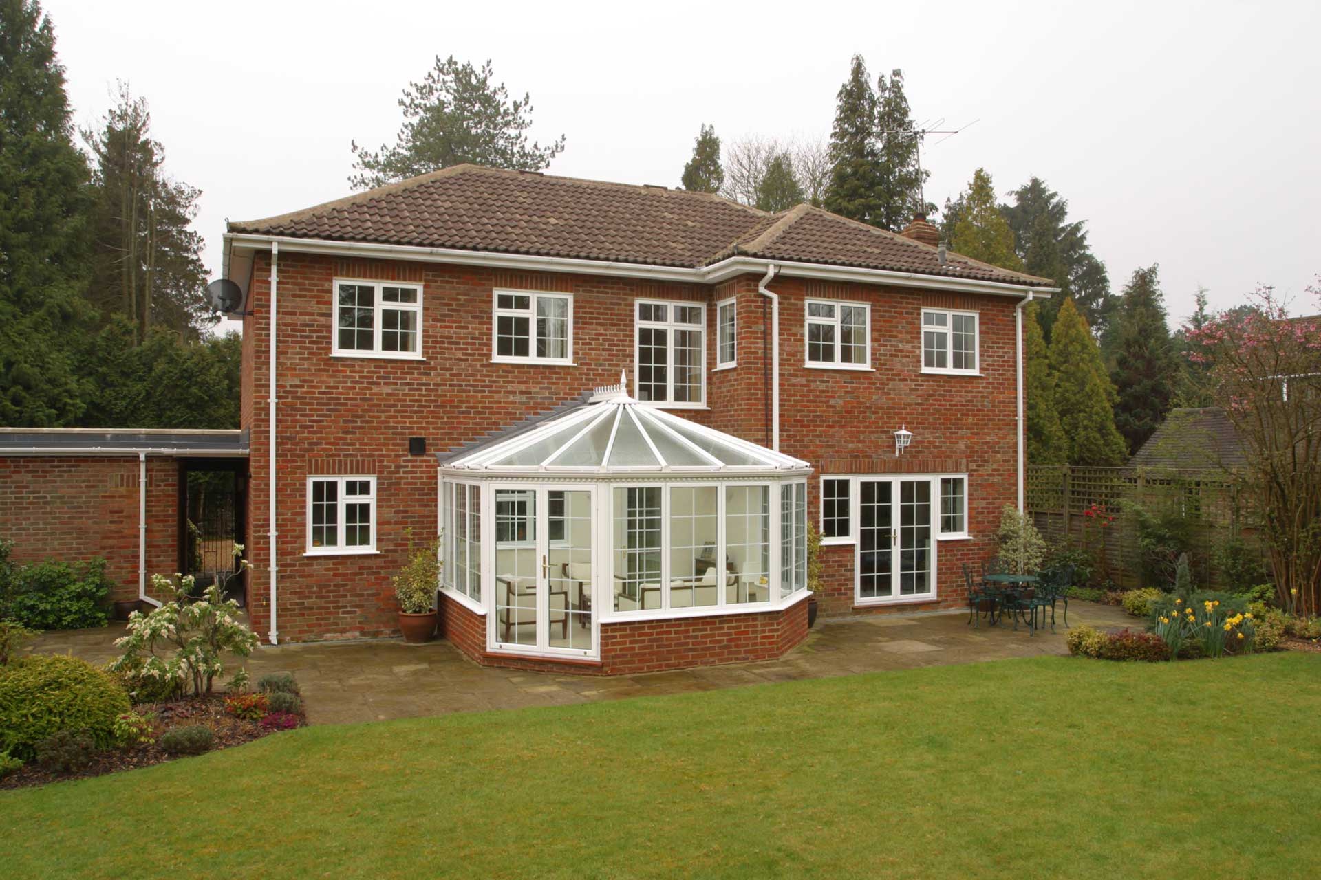 Brick home with a conservatory extension with white aluminium French doors to a back garden